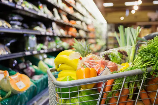 Shopping cart overflowing with fresh vegetables and fruits in a grocery store aisle