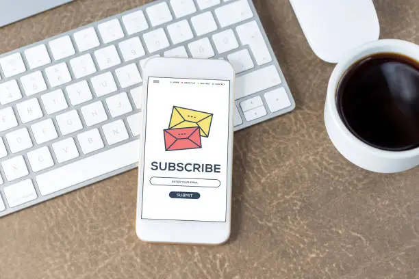 Smartphone displaying an email subscription screen with a 'Subscribe' button, placed next to a keyboard and a cup of coffee on a desk, symbolizing a user-friendly newsletter sign-up process.